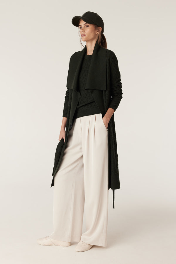 Woman in moss green Merino wool cardigan with diamond cable stitch, Milano collar, and detachable belt.