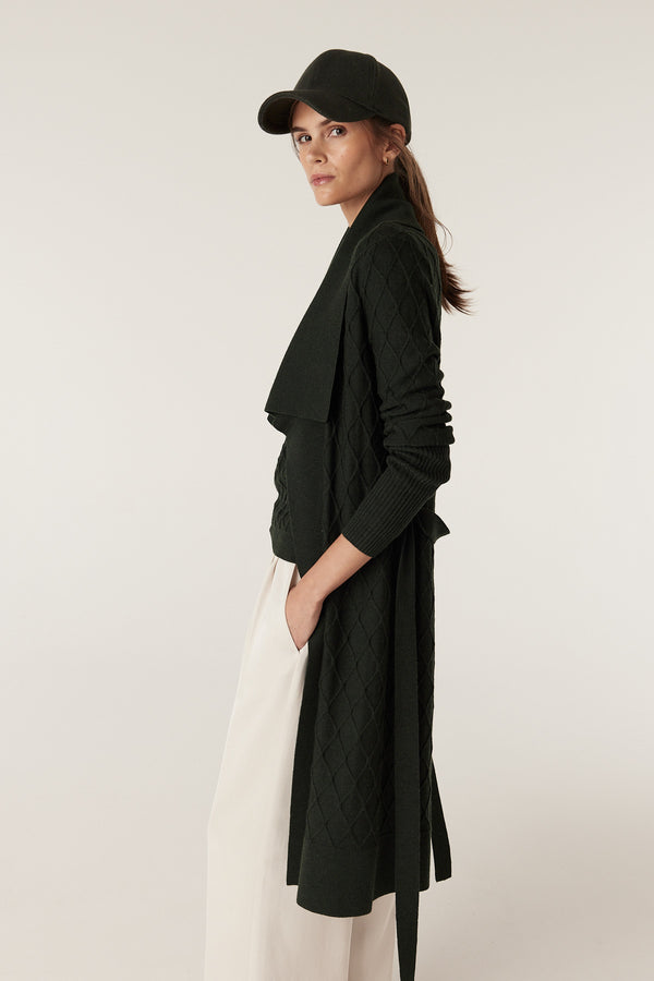 Woman in a moss green Merino wool cardigan with diamond cable stitch, Milano collar, and detachable belt.
