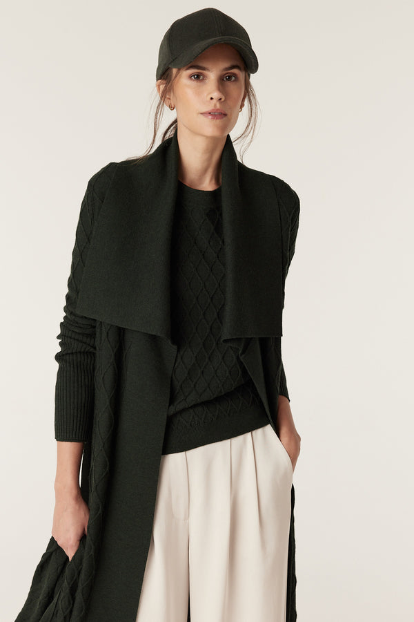 Woman in moss green Merino wool cardigan with diamond cable stitch, Milano collar, and matching cap.