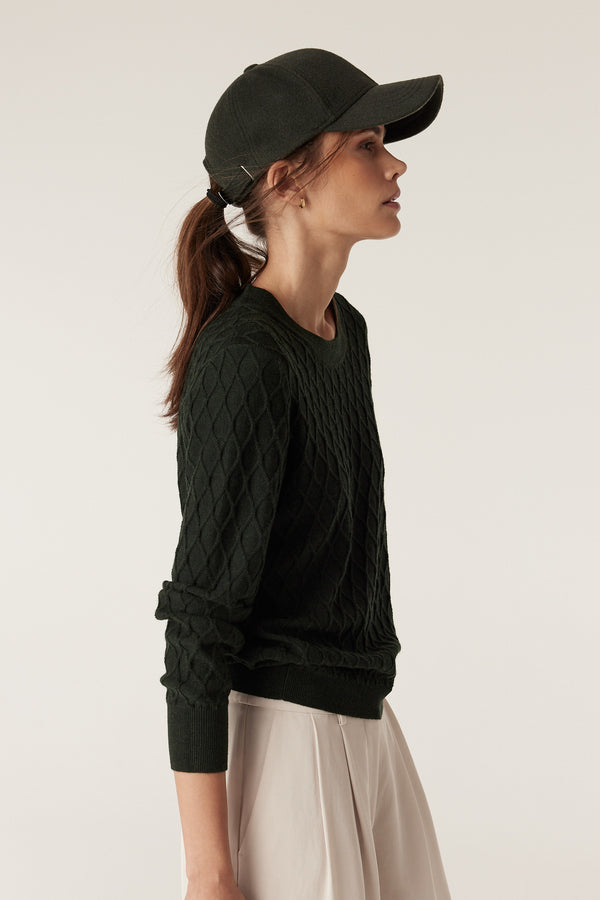 Woman in a moss green Merino wool jumper with diamond cable stitching, crew neck, and rib trims.