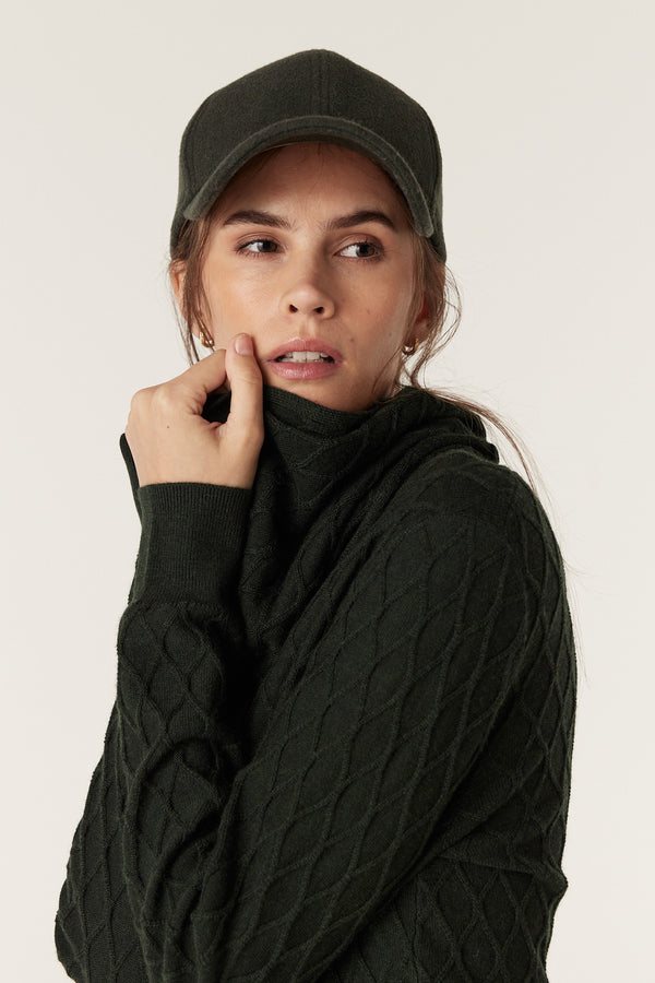 Woman wearing a moss green merino wool snood with diamond cable stitching and a matching cap.