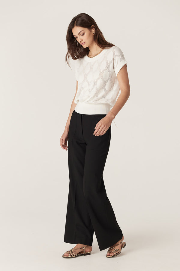 Woman in a white Silk Tencel Wave Knit Top with pointelle stitch detail, black pants, and sandals.