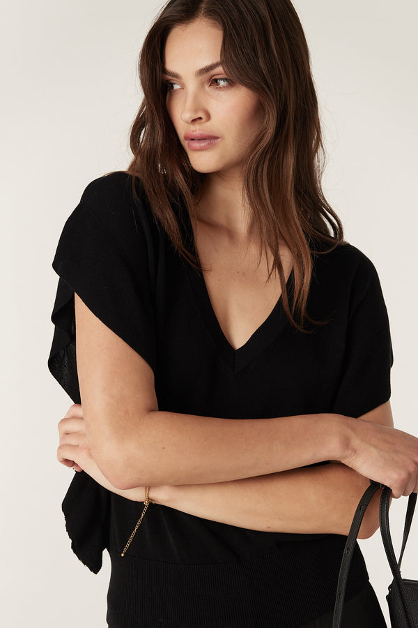 Woman wearing a black Silk Tencel V-neck frill top with ribbed trim, slim at the waist.