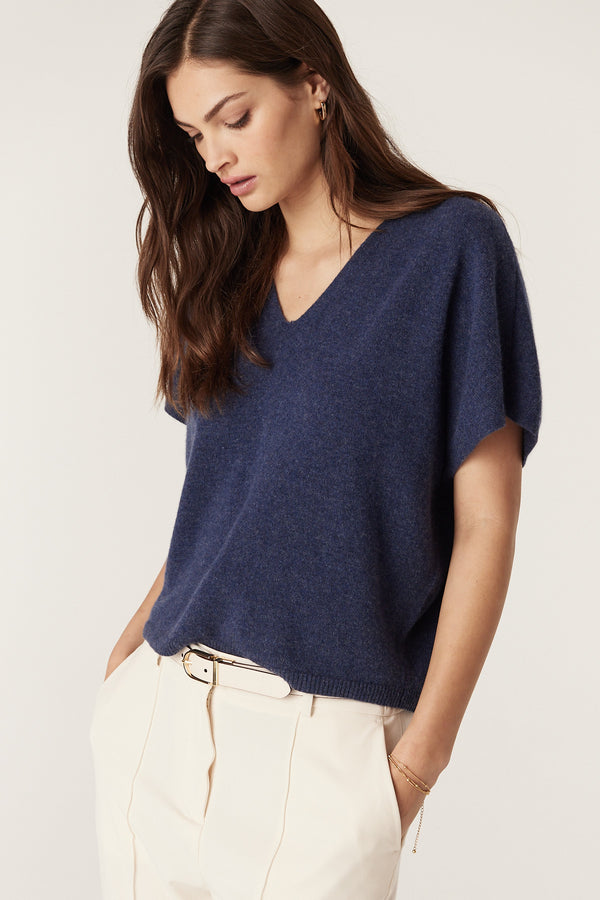 Woman wearing a denim blue pure cashmere relaxed fit V-neck top with cream pants and belt.