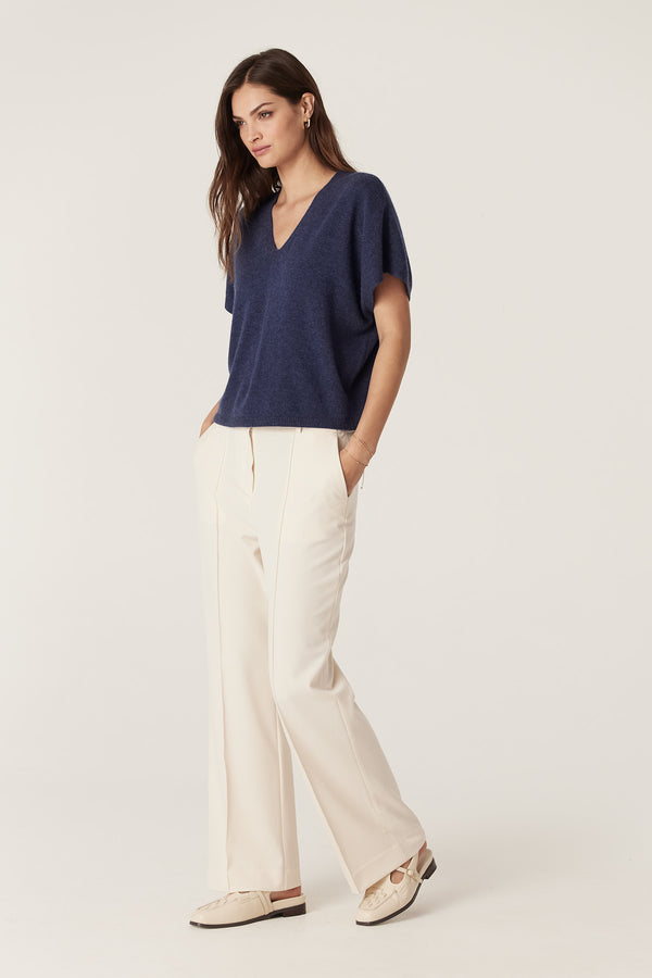 Woman in a relaxed fit denim blue cashmere V-neck top with cream wide-leg pants and light shoes.