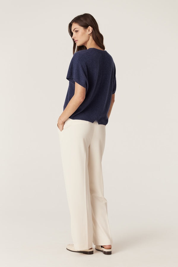 Woman wearing a relaxed fit denim blue cashmere V-neck top with a back seam, paired with cream trousers.