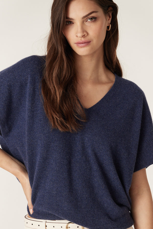 Woman in a relaxed fit denim blue cashmere V-neck top with a subtle hem split.