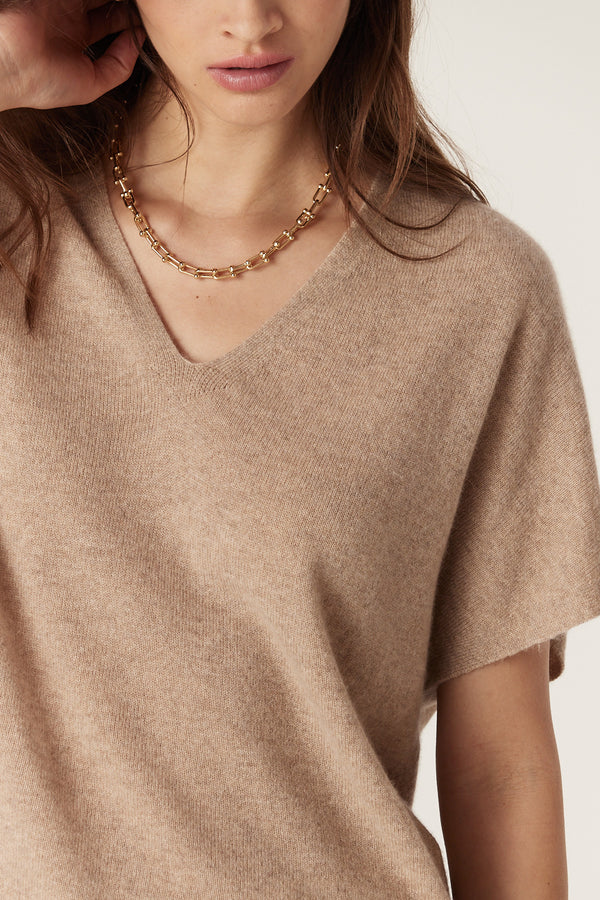 Close-up of a woman wearing a biscuit pure cashmere relaxed fit V-neck top with a gold chain necklace.