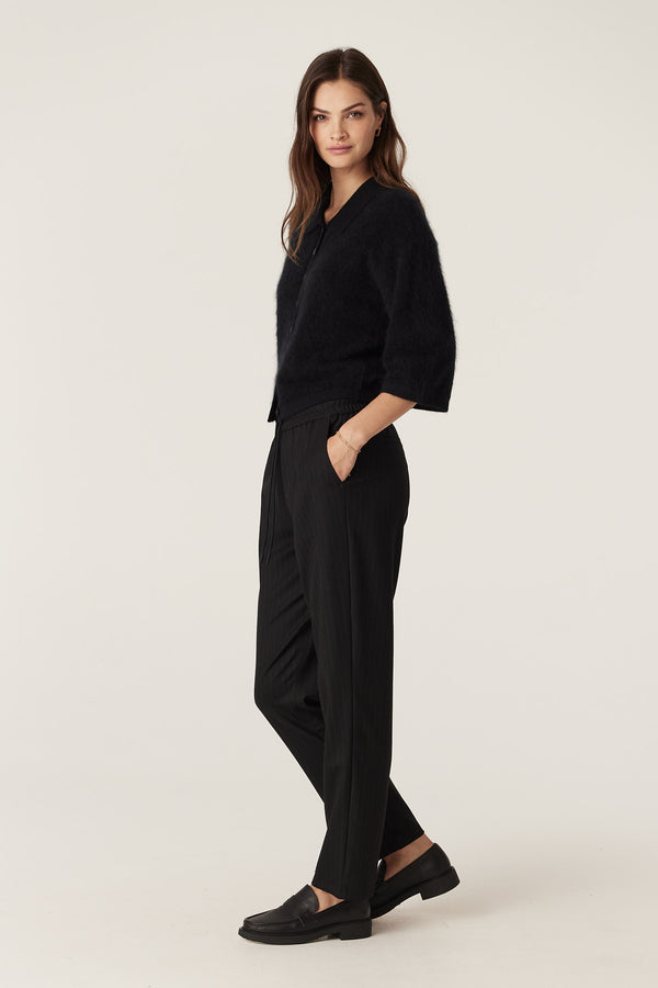 Woman in a black brushed cashwool polo cardigan with flared cropped sleeves and black pinstripe pants.