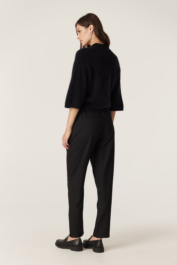 Woman in a black brushed cashwool polo cardigan with flared cropped sleeves, paired with pinstripe trousers.