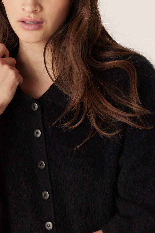 Close-up of a woman wearing a black brushed cashwool polo cardigan with a button-front and soft texture.