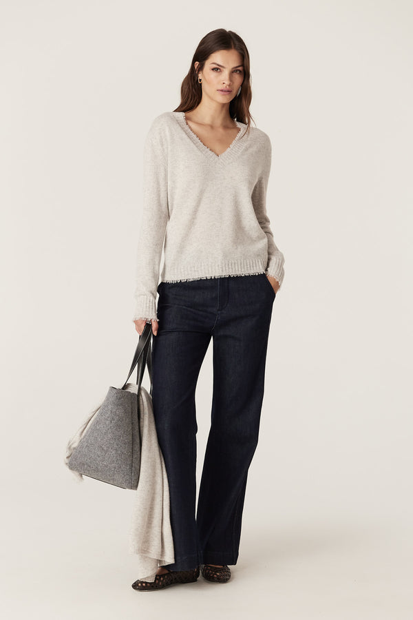 Woman in frost Cashwool Aura V-neck jumper with loop fringing, dark jeans, and a grey tote bag.