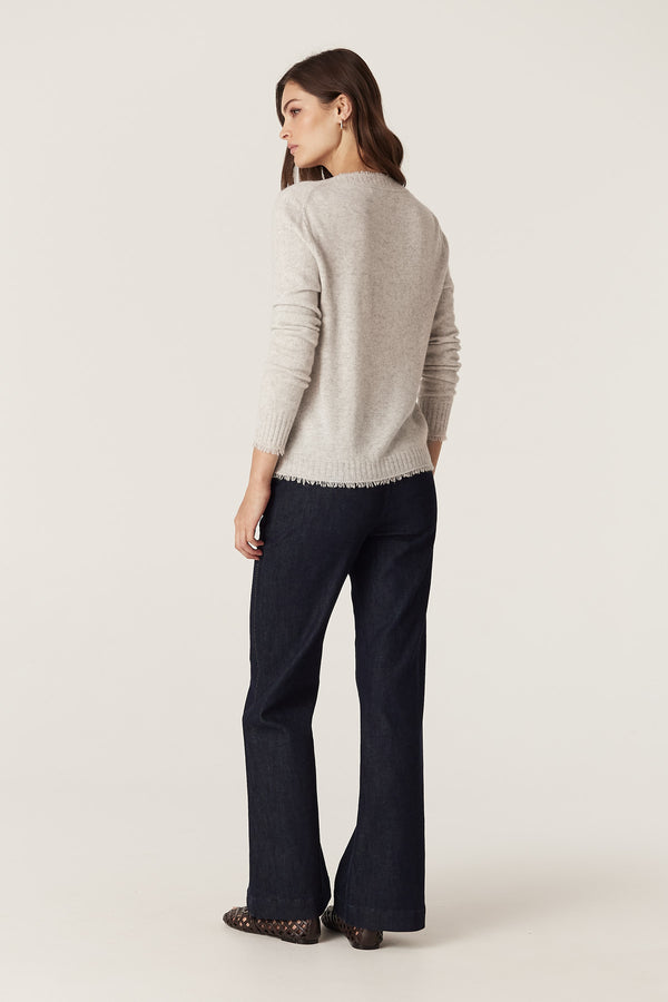 Woman in a frost Cashwool Aura Jumper with V-neck and fringed rib trims, paired with dark jeans.