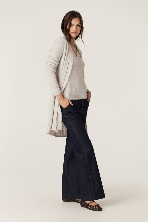 Woman in a frost Cashwool Aura Cardigan with fringing, light knit top, and dark flare jeans.