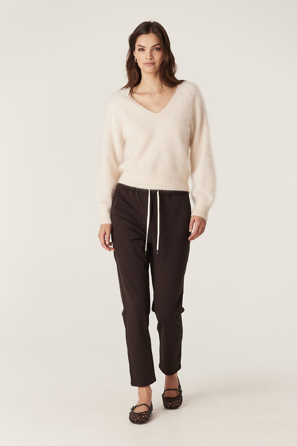 Model wears a parchment brushed cashwool V-neck jumper with ribbed cuffs and hem, paired with dark trousers.