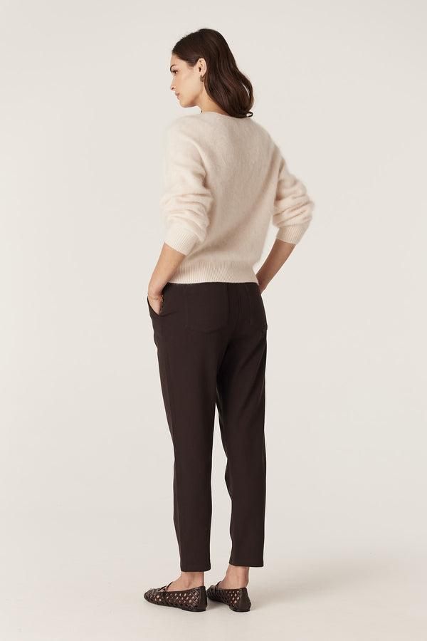 Woman in a parchment brushed cashwool V-neck jumper and dark trousers, hands in pockets.