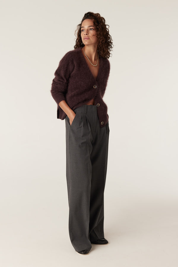 Woman wearing a brushed Shiraz cashwool V-neck cardigan with gold buttons and grey pleated trousers.