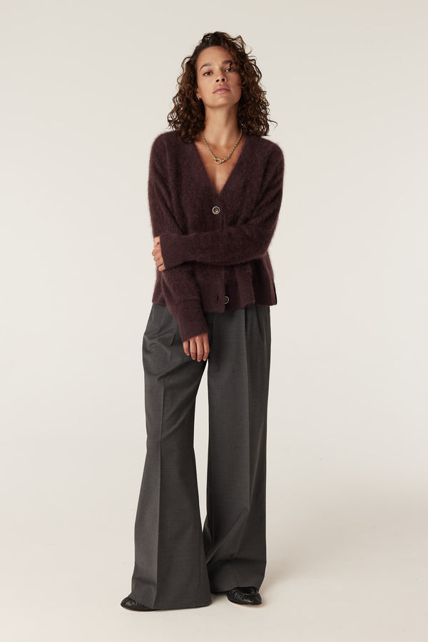 Woman wearing a shiraz brushed cashwool V-neck cardigan with a single button closure, paired with grey wide-leg trousers.