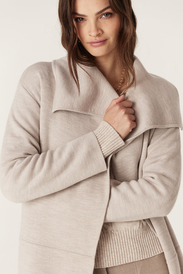 Woman wearing a mushroom Parsons Merino longline cardigan with wide collar, side pockets, and ribbed cuffs.