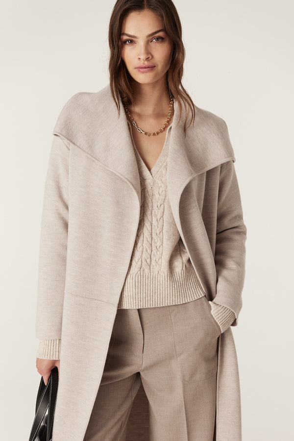 Woman wearing a mushroom Parsons Merino longline cardigan over a cable knit sweater and trousers.