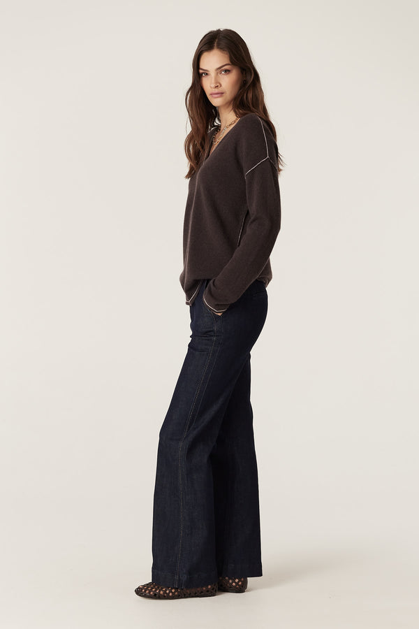 Model wears a chocolate pure cashmere V-neck jumper with contrast stitching and dark wash jeans.