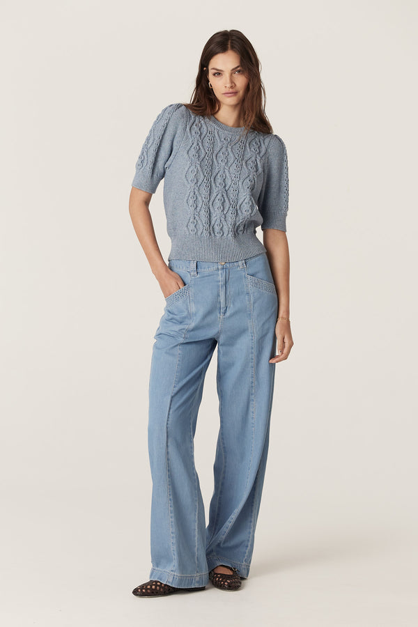 Woman in dusty blue Tavi Knit Top with cable stitch, tucks at sleeve head, and light wash denim pants.