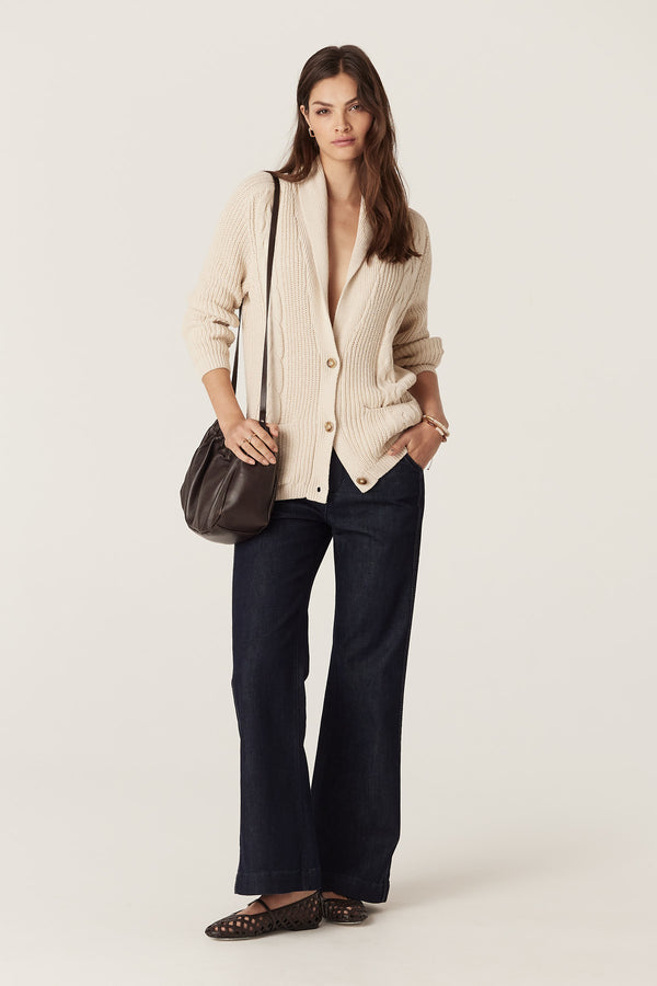 Woman in an oatmeal cotton linen blend Grandpa Cable Cardigan with shawl collar, buttons, and patch pockets.