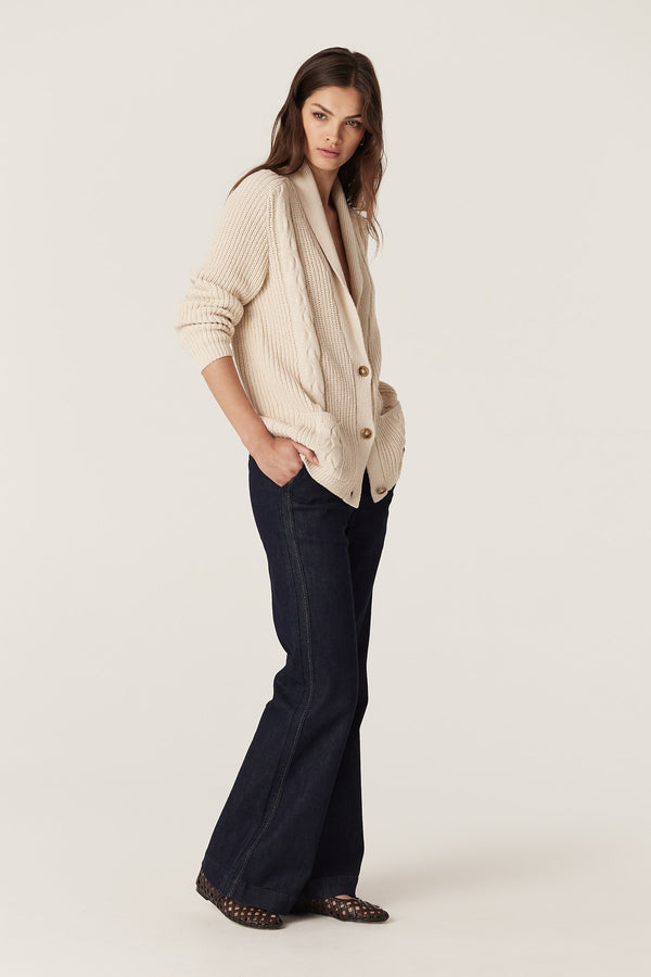 Woman in an oatmeal cotton linen Grandpa Cable Cardigan with shawl collar, button front, and patch pockets.