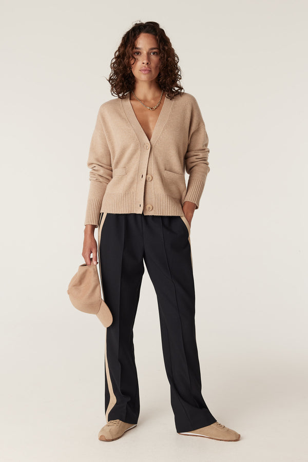 Woman wearing a camel Cashwool V-neck cardigan with front buttons and pockets, paired with dark pants.
