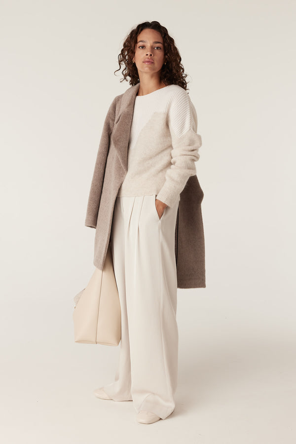 Woman in oatmeal boat neck knit jumper, cream wide-leg trousers, and a taupe coat.
