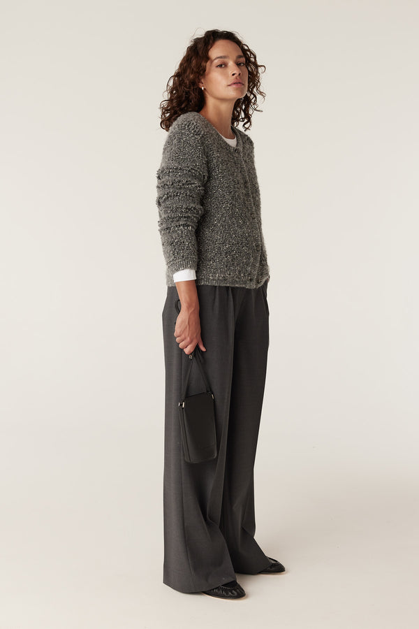 Model wearing an ash grey teddy knit cardigan over a white tee, paired with dark grey wide-leg trousers.
