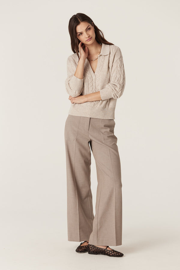 Woman in a sand Cashwool cable knit polo jumper with a V-neck, paired with taupe wide-leg trousers.