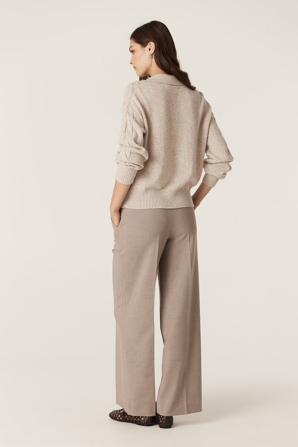 Woman in a sand Cashwool cable knit polo jumper with rib trims and wide-leg trousers.