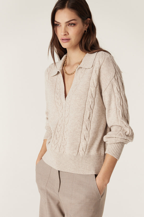 Woman wearing a sand Cashwool cable knit polo jumper with a V-neck and ribbed trims.