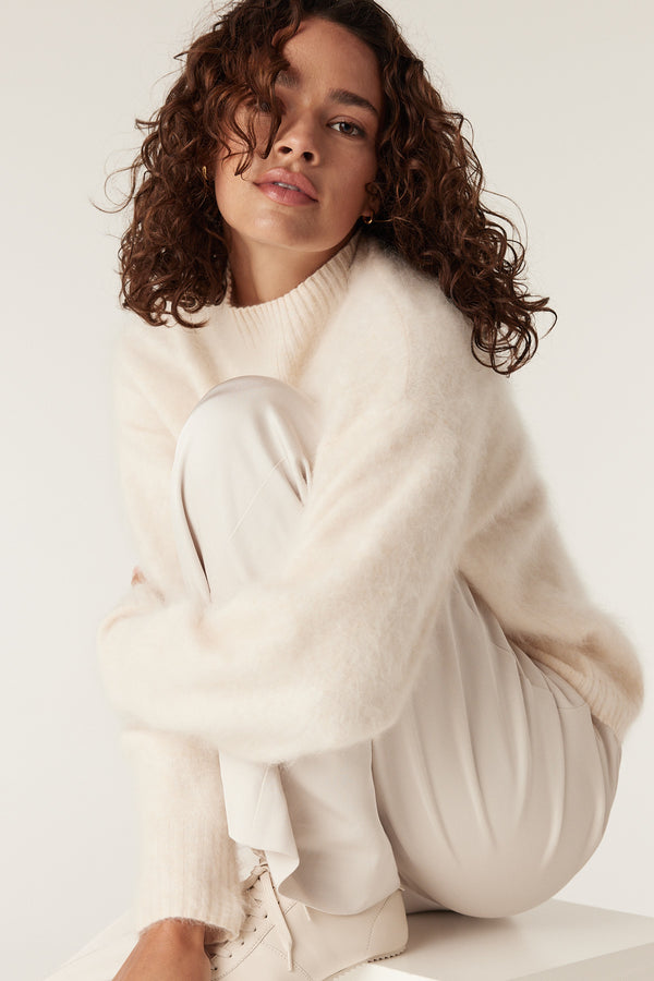 Woman wearing a soft parchment brushed cashwool turtle neck jumper and light trousers.