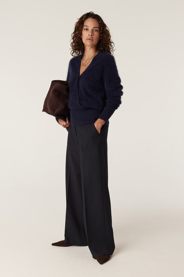 Woman wearing a navy brushed cashwool jumper, dark wide-leg trousers, and holding a brown bag.