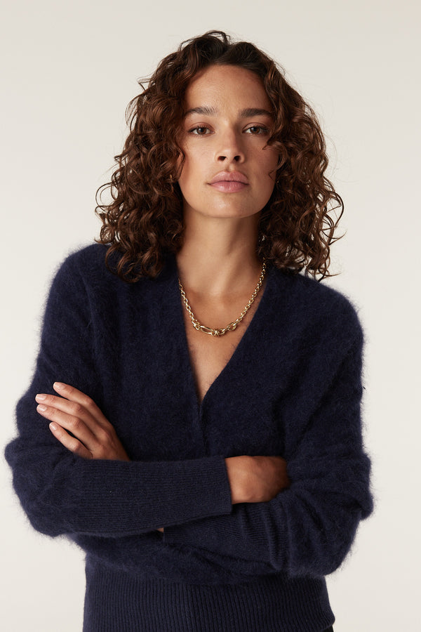 Woman wearing a navy brushed cashwool jumper with a V-neck and ribbed cuffs.
