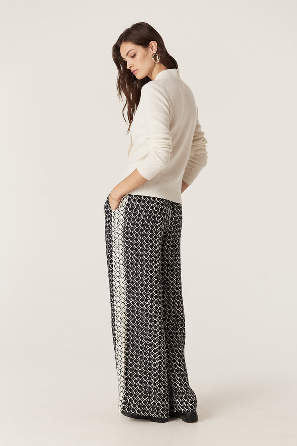 Woman in a milk-colored Cashwool Tie Jumper with a turtle neck and rib knit, paired with patterned pants.