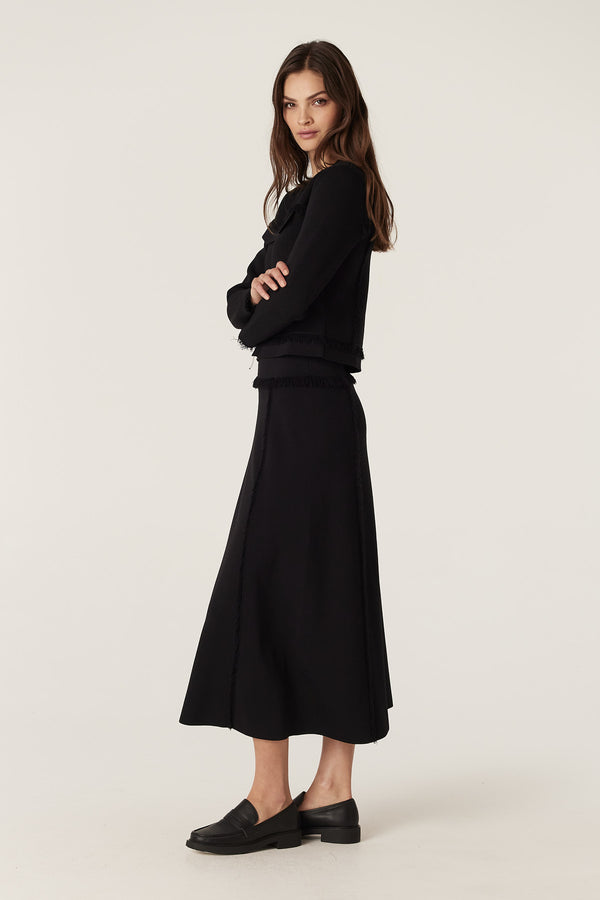 Woman in black crepe fringe jacket with crew neck and matching midi skirt.