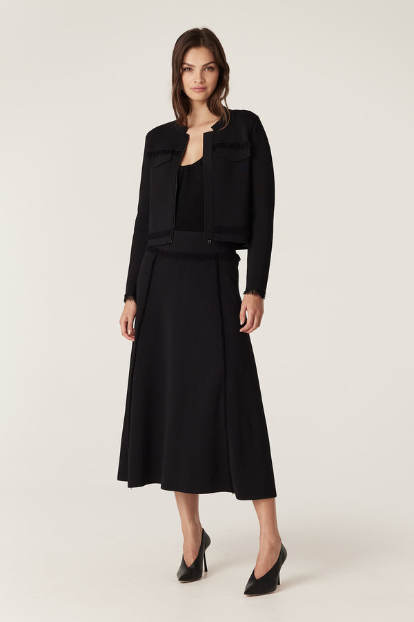 Woman in black Crepe Fringe Jacket and matching skirt, featuring Milano knit, fringe details, and faux pocket flaps.