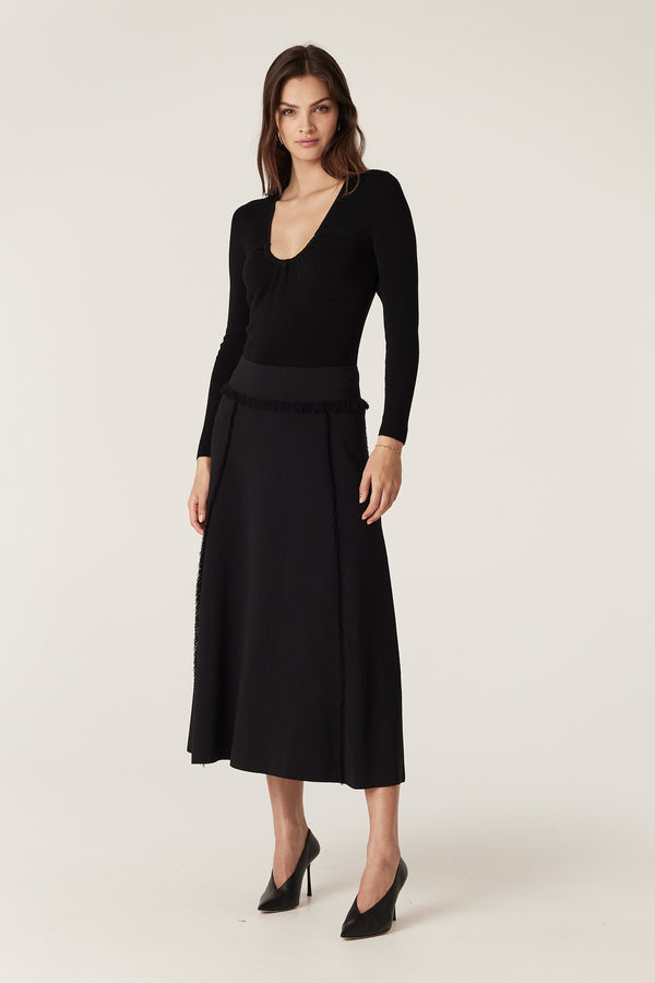 Model wears a black crepe fringe midi skirt with a heavyweight Milano knit and fringe detailing.