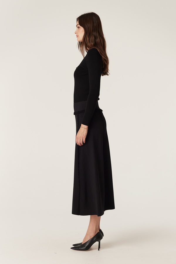 Woman in a black crepe fringe midi skirt with a Milano knit texture and a long-sleeved top.