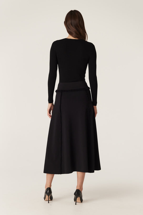 Black Milano knit midi skirt with fringe details on seams, worn by a model from behind.