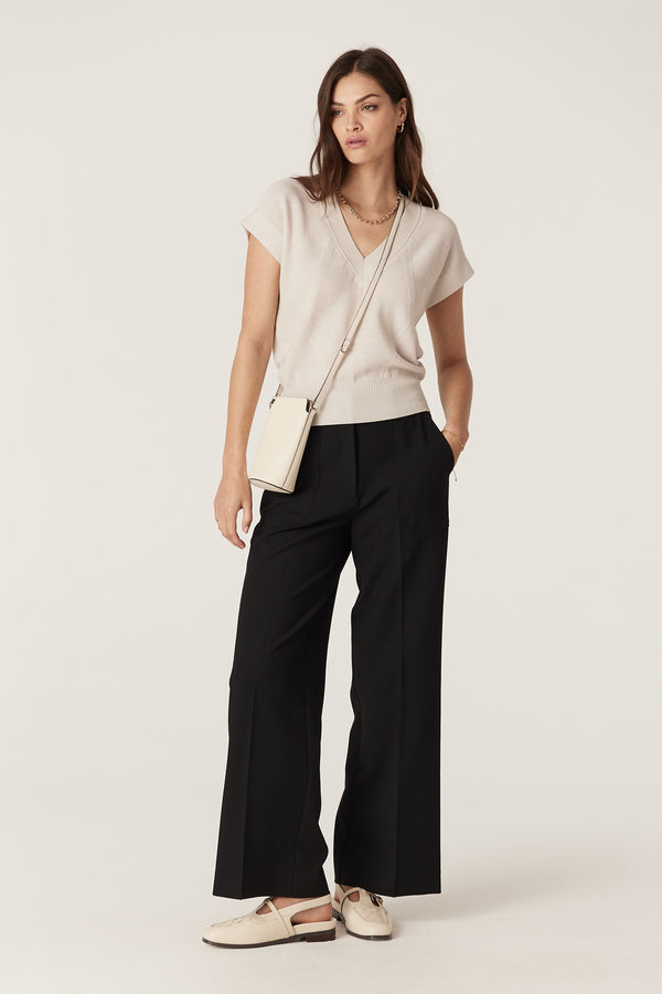 Woman in an antique white merino wool V-neck top, black wide-leg pants, and a small cream cross-body bag.