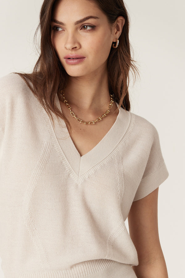 Woman wearing an antique white merino wool V-neck top with moss stitch and rib details.