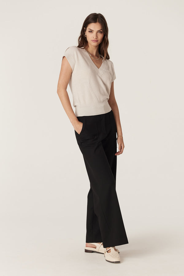 Woman in an antique white merino wool V-neck top with moss stitch and black pants.