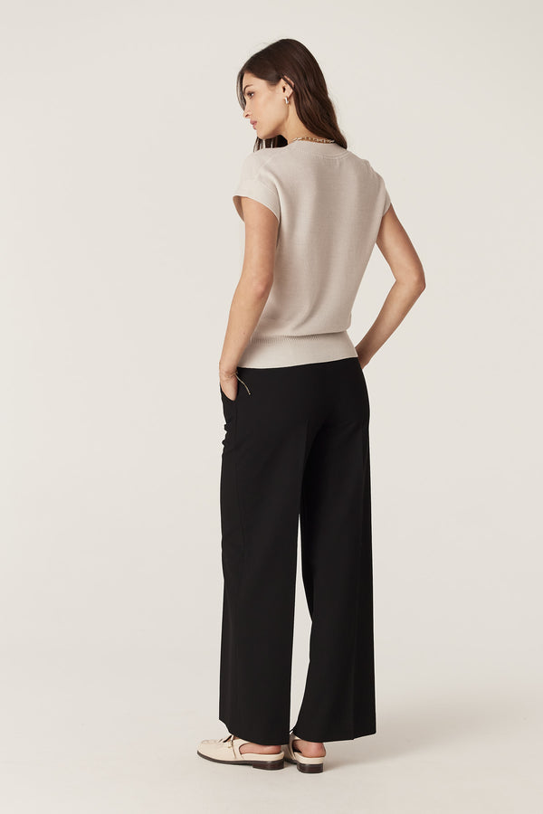 Woman wearing an antique white merino wool V-neck top with moss stitch and black wide-leg pants.