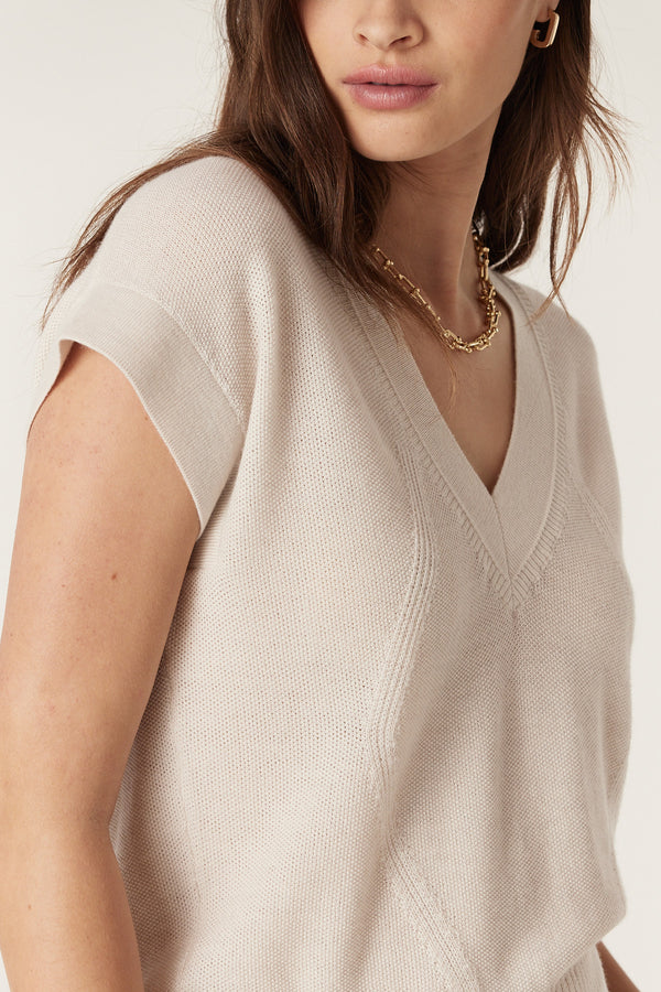 Woman wearing an antique white merino wool V-neck top with moss stitch and rib details.