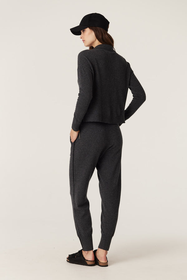 Woman in charcoal Cashwool track pants with cord detail, matching knit top, black cap, and sandals.