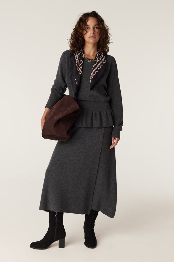 Woman in charcoal merino knit skirt and matching top, carrying a brown suede bag.